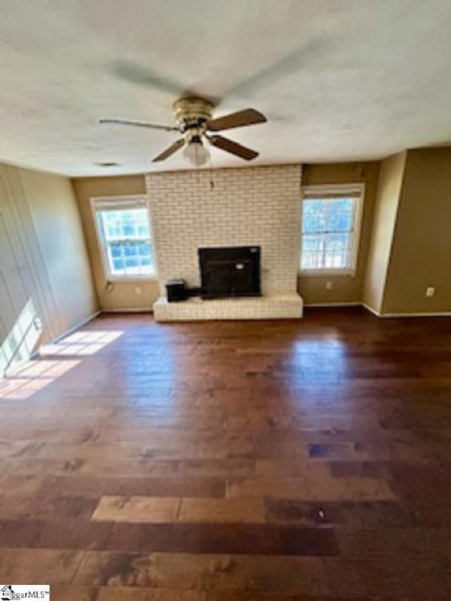 unfurnished living room featuring a healthy amount of sunlight, a fireplace, wood finished floors, and a ceiling fan