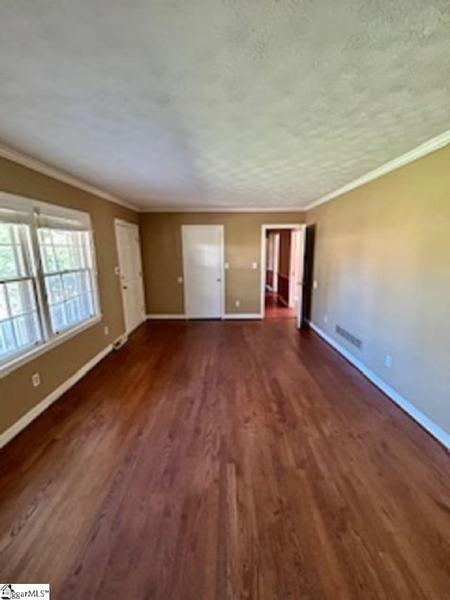 interior space featuring dark wood-style flooring, ornamental molding, baseboards, a textured ceiling, and visible vents