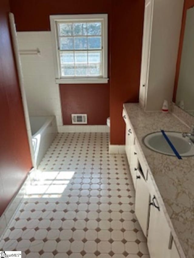 full bathroom featuring visible vents, a washtub, baseboards, toilet, and vanity