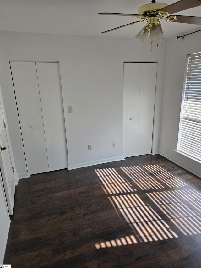 unfurnished bedroom with a ceiling fan, dark wood-type flooring, baseboards, and multiple closets