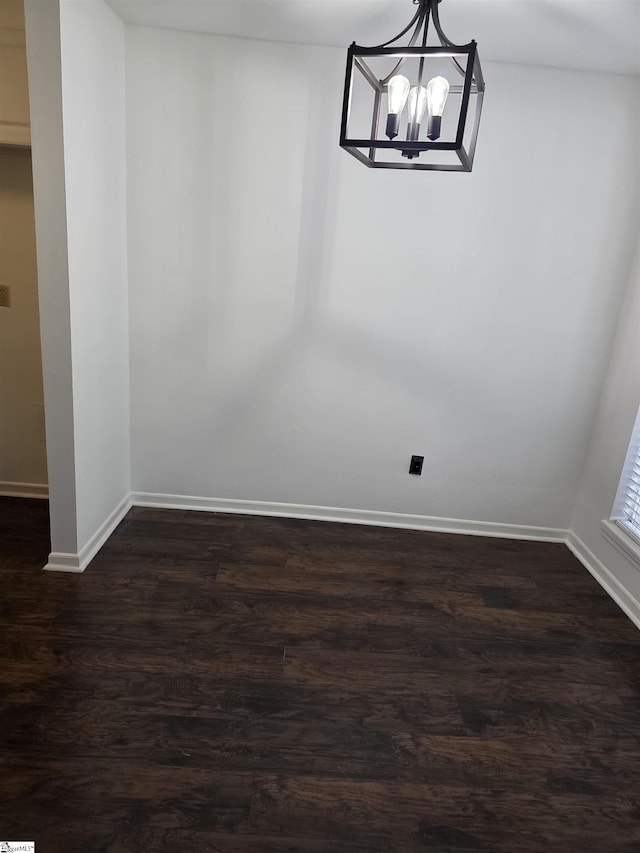unfurnished dining area featuring baseboards, an inviting chandelier, and dark wood finished floors