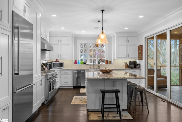 kitchen featuring crown molding, light stone countertops, under cabinet range hood, white cabinetry, and premium appliances