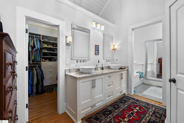 full bath with lofted ceiling, a sink, double vanity, and wood finished floors