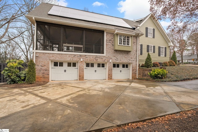 exterior space with roof with shingles, concrete driveway, brick siding, roof mounted solar panels, and a garage