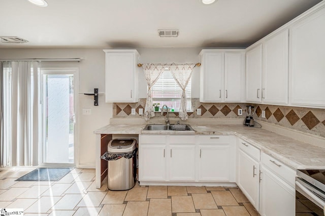 kitchen featuring white cabinets, visible vents, light countertops, a sink, and backsplash