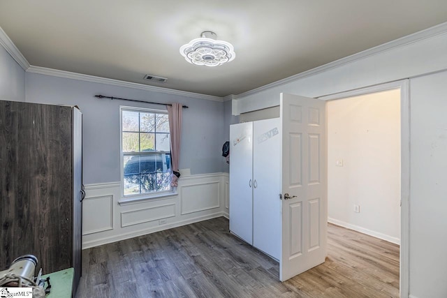 unfurnished bedroom with visible vents, ornamental molding, wood finished floors, and wainscoting