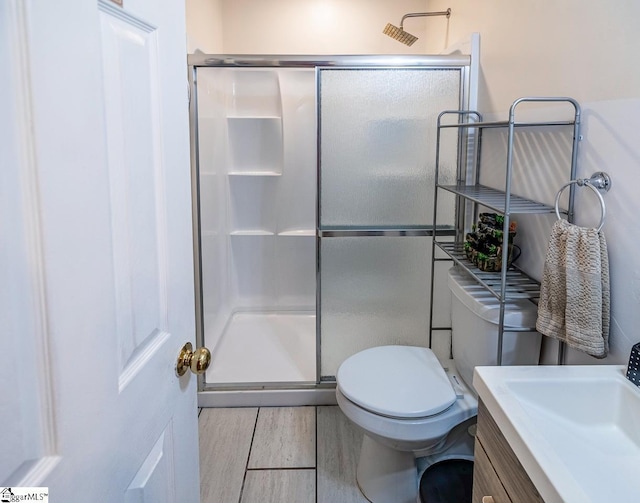 bathroom with a shower stall, toilet, vanity, and wood finish floors