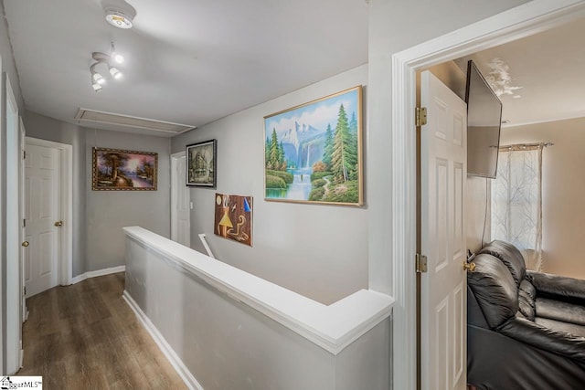 hallway with an upstairs landing, baseboards, attic access, and dark wood finished floors