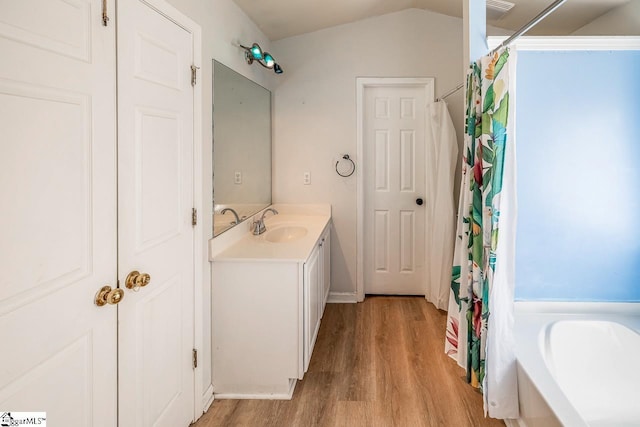 bathroom featuring vanity, lofted ceiling, a bathtub, visible vents, and wood finished floors