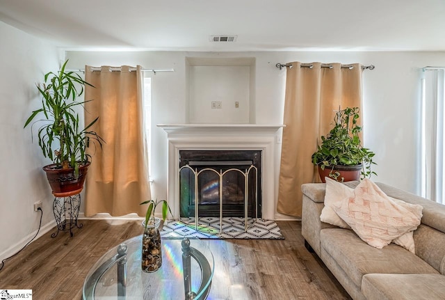 living room featuring visible vents, baseboards, a fireplace, and wood finished floors