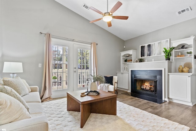 living room with light wood finished floors, a warm lit fireplace, lofted ceiling, visible vents, and ceiling fan