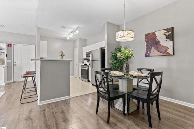 dining area featuring baseboards, visible vents, light wood-style floors, and rail lighting