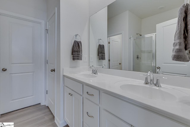bathroom with double vanity, a sink, a stall shower, and wood finished floors