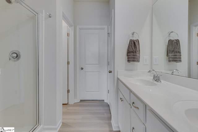 full bathroom with a stall shower, double vanity, wood finished floors, and a sink