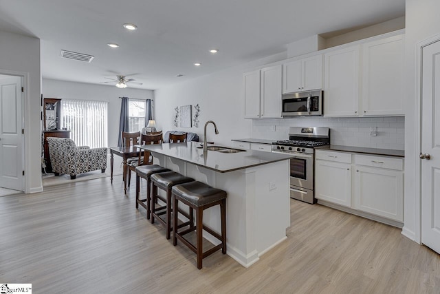kitchen featuring a sink, a kitchen bar, a center island with sink, stainless steel appliances, and visible vents