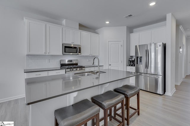 kitchen featuring visible vents, light wood finished floors, stainless steel appliances, tasteful backsplash, and a kitchen breakfast bar
