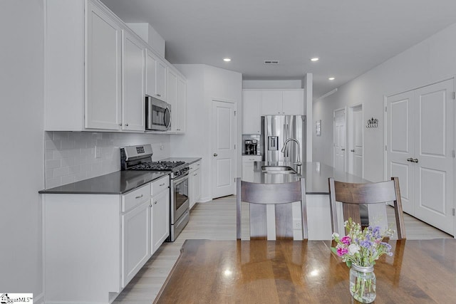 kitchen featuring white cabinets, visible vents, dark countertops, appliances with stainless steel finishes, and a sink