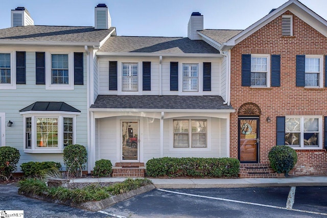 view of front of house with uncovered parking, a chimney, brick siding, and roof with shingles
