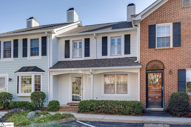 multi unit property with uncovered parking, a chimney, brick siding, and roof with shingles