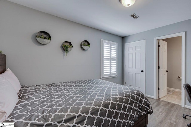bedroom with connected bathroom, baseboards, visible vents, and wood finished floors