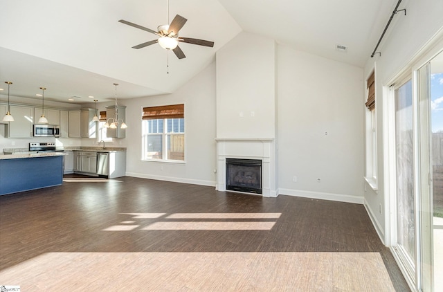 unfurnished living room featuring plenty of natural light, a fireplace, a sink, and high vaulted ceiling