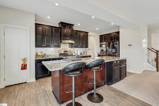 kitchen featuring a sink, a kitchen bar, appliances with stainless steel finishes, light wood-type flooring, and under cabinet range hood