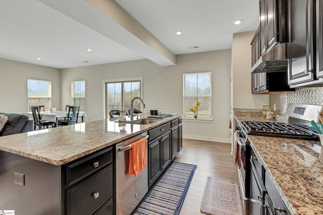 kitchen featuring a sink, light wood-style flooring, under cabinet range hood, stainless steel appliances, and visible vents