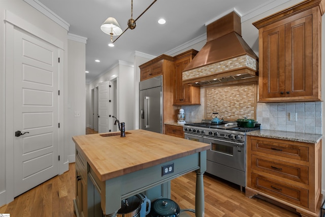 kitchen with wood finished floors, butcher block countertops, premium appliances, premium range hood, and ornamental molding
