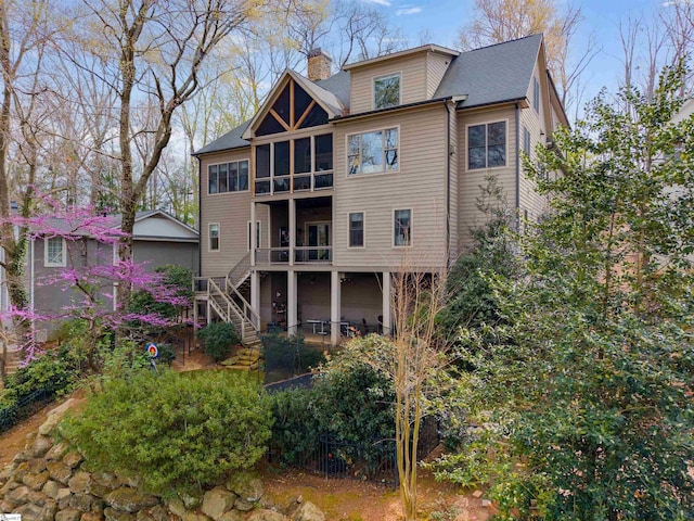 back of house featuring a sunroom, a chimney, stairs, and a shingled roof