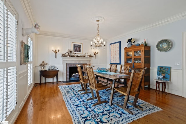 dining space featuring light wood finished floors, ornamental molding, a decorative wall, and a chandelier