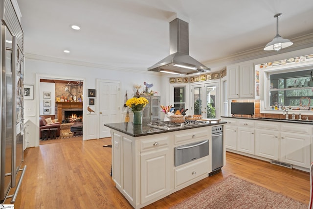 kitchen with island exhaust hood, crown molding, appliances with stainless steel finishes, a lit fireplace, and a warming drawer