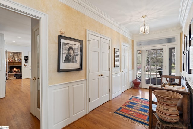 interior space featuring a wainscoted wall, an inviting chandelier, light wood-style floors, and crown molding