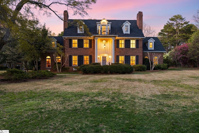 colonial house featuring a balcony, a chimney, a front yard, and brick siding