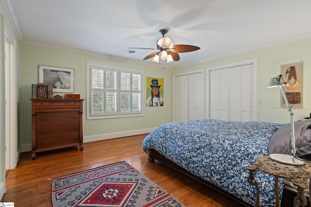 bedroom with two closets, ornamental molding, baseboards, ceiling fan, and wood finished floors