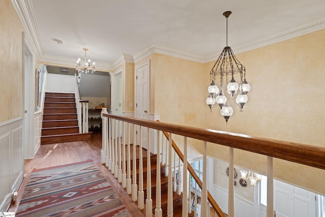 hallway with stairs, wood finished floors, ornamental molding, and an inviting chandelier
