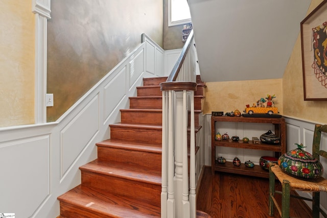 stairs with a decorative wall, wood finished floors, and wainscoting