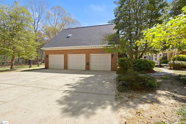 view of side of property with brick siding, a garage, driveway, and a shingled roof