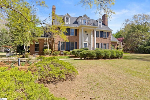 greek revival house featuring brick siding, a front lawn, and a chimney