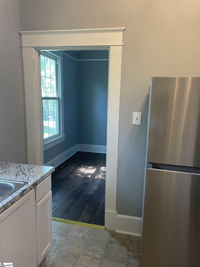 kitchen with light stone countertops, white cabinets, freestanding refrigerator, and baseboards