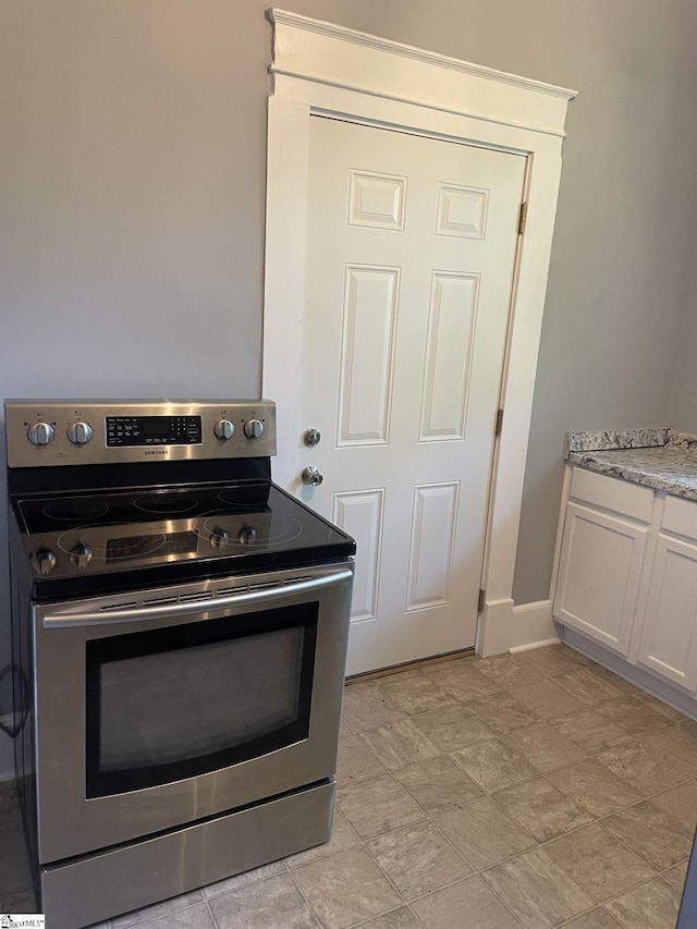 kitchen featuring stainless steel electric stove, white cabinets, and baseboards