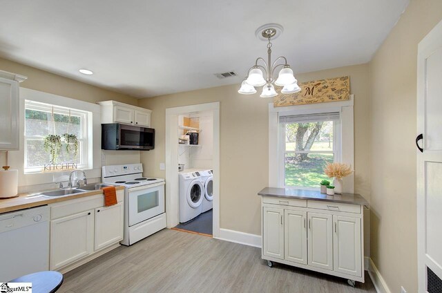 kitchen featuring visible vents, white appliances, a sink, an inviting chandelier, and washer and clothes dryer