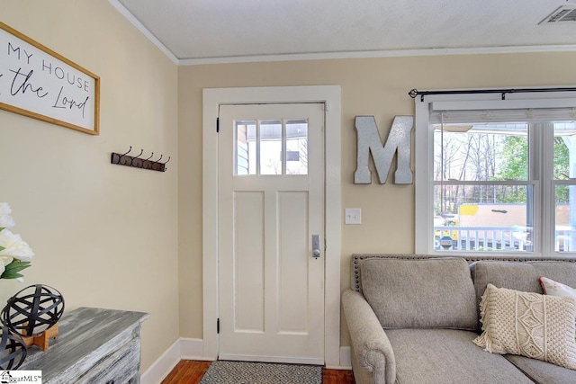 entryway with wood finished floors, ornamental molding, baseboards, and visible vents