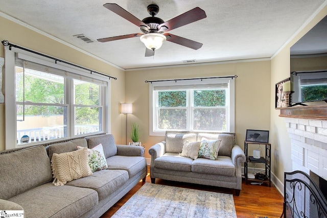 living room with a textured ceiling, ornamental molding, visible vents, and wood finished floors