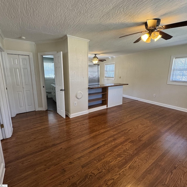unfurnished living room with crown molding, a textured ceiling, baseboards, ceiling fan, and dark wood-style flooring