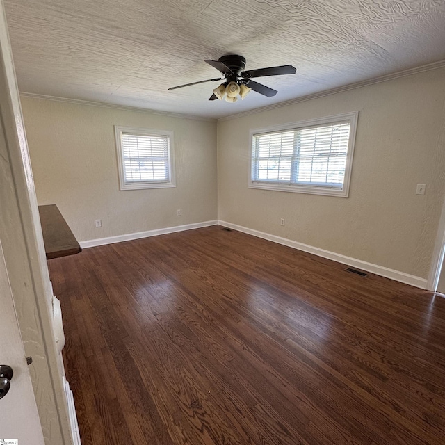 unfurnished room with plenty of natural light, visible vents, crown molding, and dark wood finished floors
