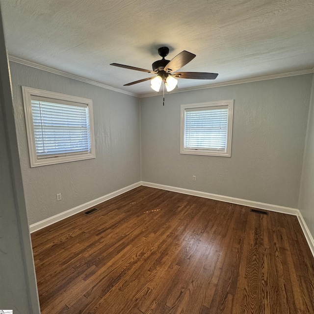 empty room featuring crown molding, dark wood-type flooring, baseboards, visible vents, and a ceiling fan