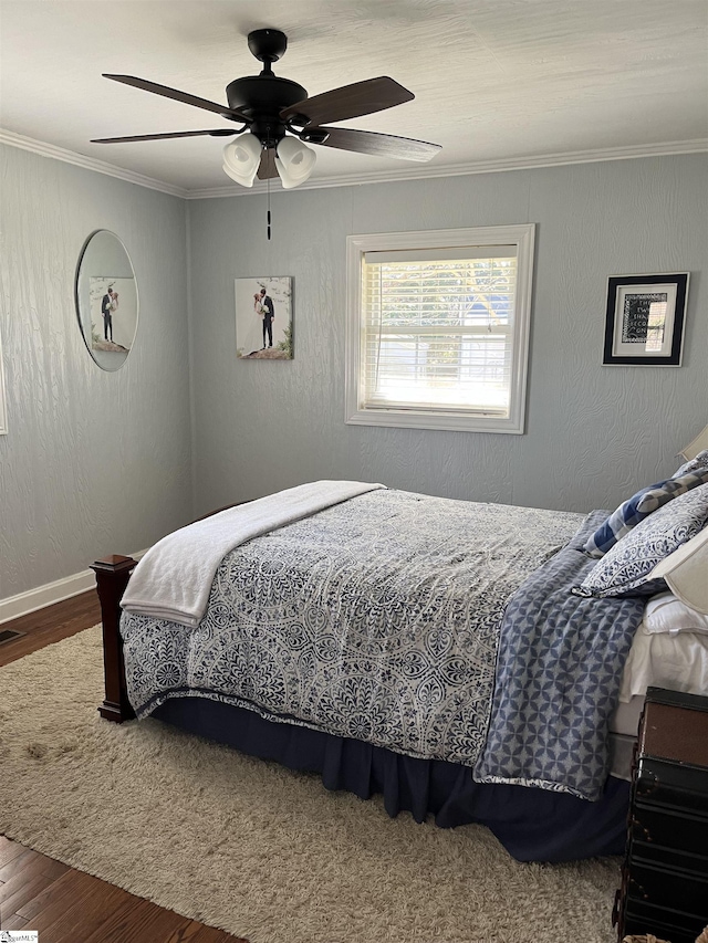 bedroom featuring a ceiling fan, wood finished floors, visible vents, ornamental molding, and a textured wall