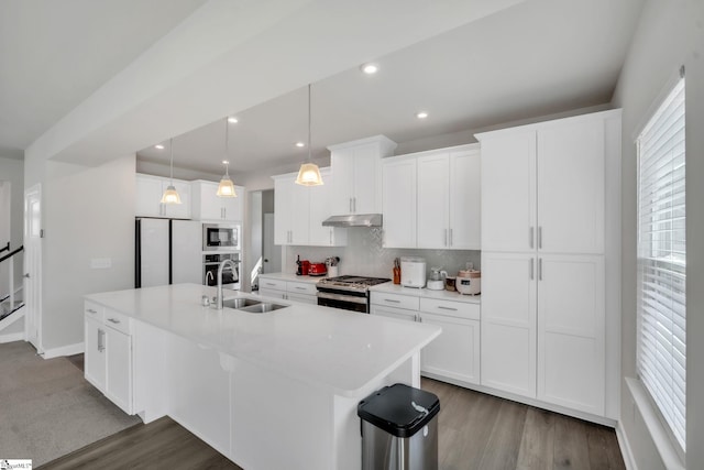 kitchen featuring decorative backsplash, appliances with stainless steel finishes, a center island with sink, wood finished floors, and a sink