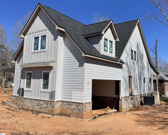 view of home's exterior with central AC unit, driveway, a shingled roof, and board and batten siding