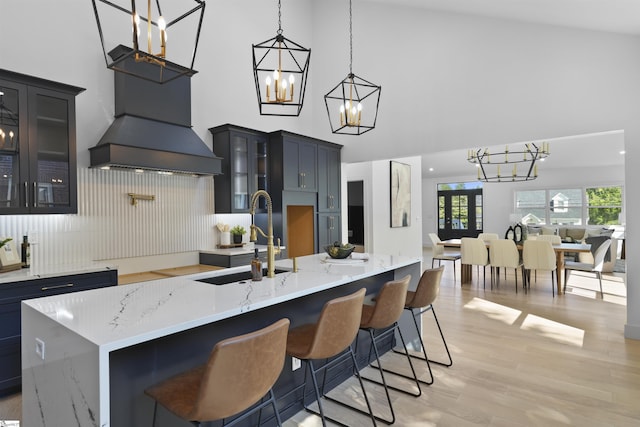 kitchen featuring a sink, a chandelier, a breakfast bar area, light wood-type flooring, and a towering ceiling